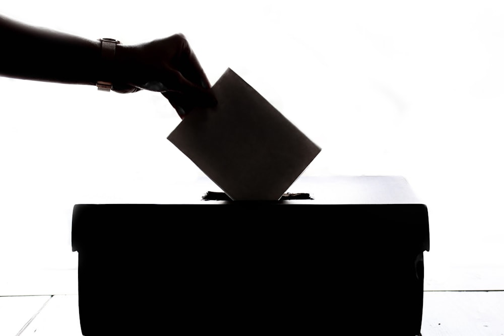 A hand casting a ballot into a ballot box